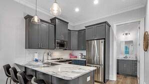 Una cocina moderna con gabinetes grises, electrodomésticos de acero inoxidable y una isla de mármol con taburetes.