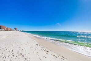 A beach with footprints leading to the water, a clear sky, and buildings in the background. - Modern 3BR Home, Pool, Steps To Beach & Lagoon, Fishing Pier, Dog Friendly (Gulf Shores)