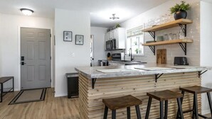 Una cucina moderna con isola in marmo, sgabelli di legno ed elettrodomestici integrati.