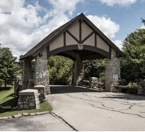 Enter a traditional lodge with a stone archway and steps leading to a paved driveway, surrounded by lush greenery.