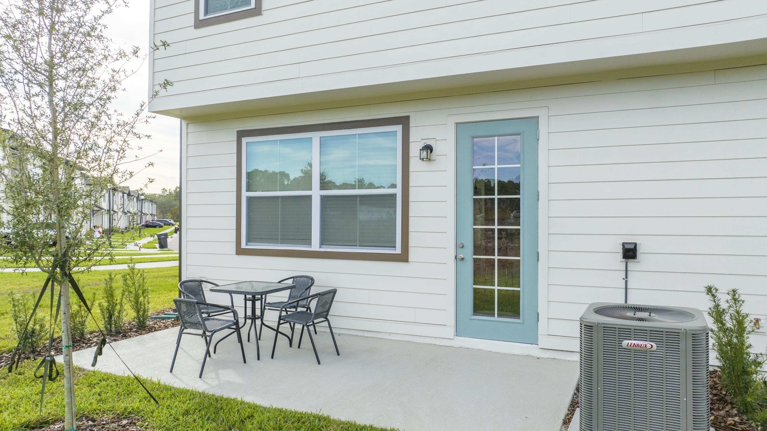 A residential building with a patio area featuring a table and chairs, a blue door, and an air conditioning unit.