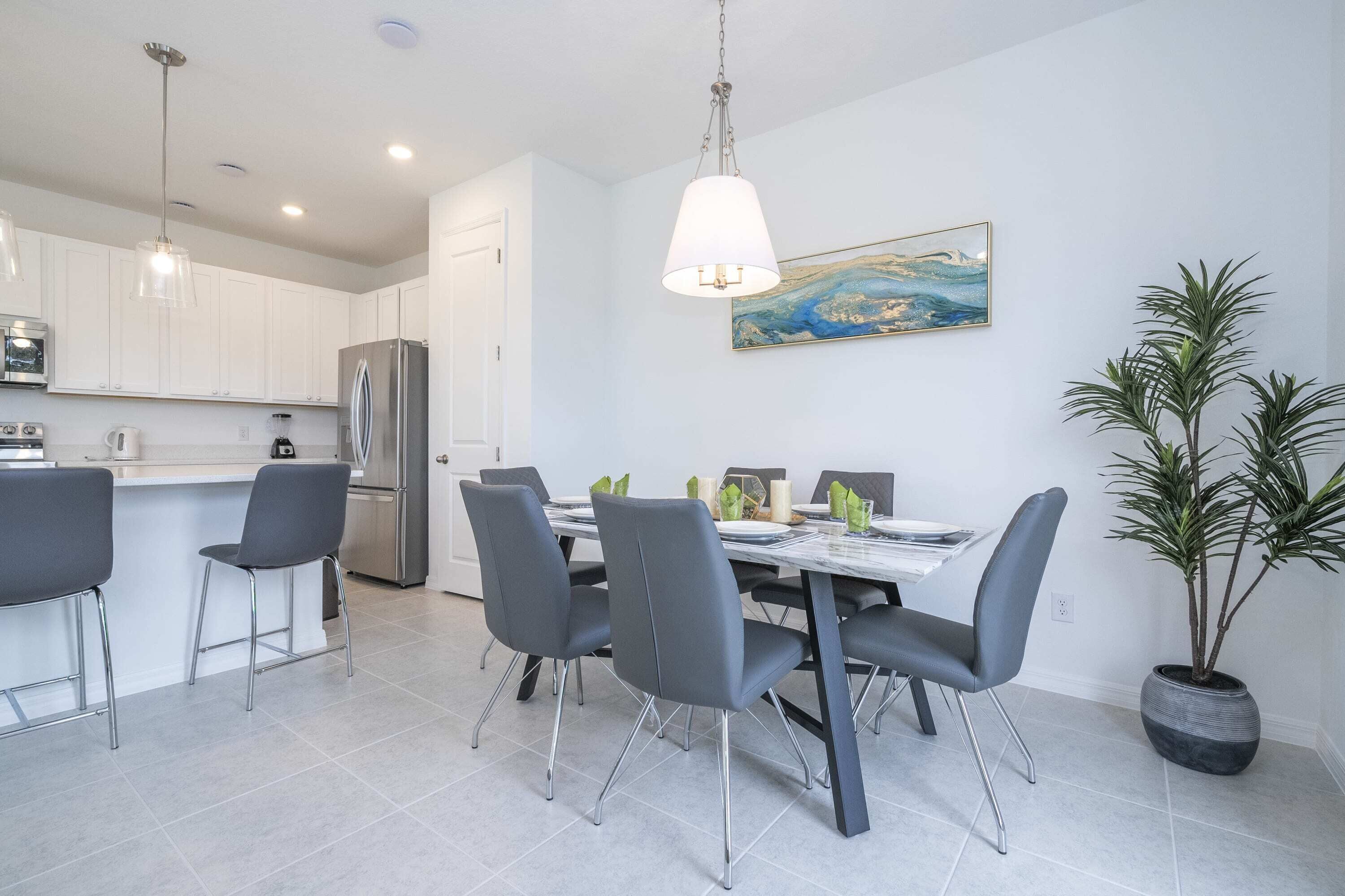 Una cocina moderna con armarios blancos, un refrigerador de acero inoxidable y un comedor con una mesa de mármol y sillas grises.