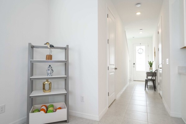 A hallway with a white door at the end, a shelf with decorative items, and a chair near the door.