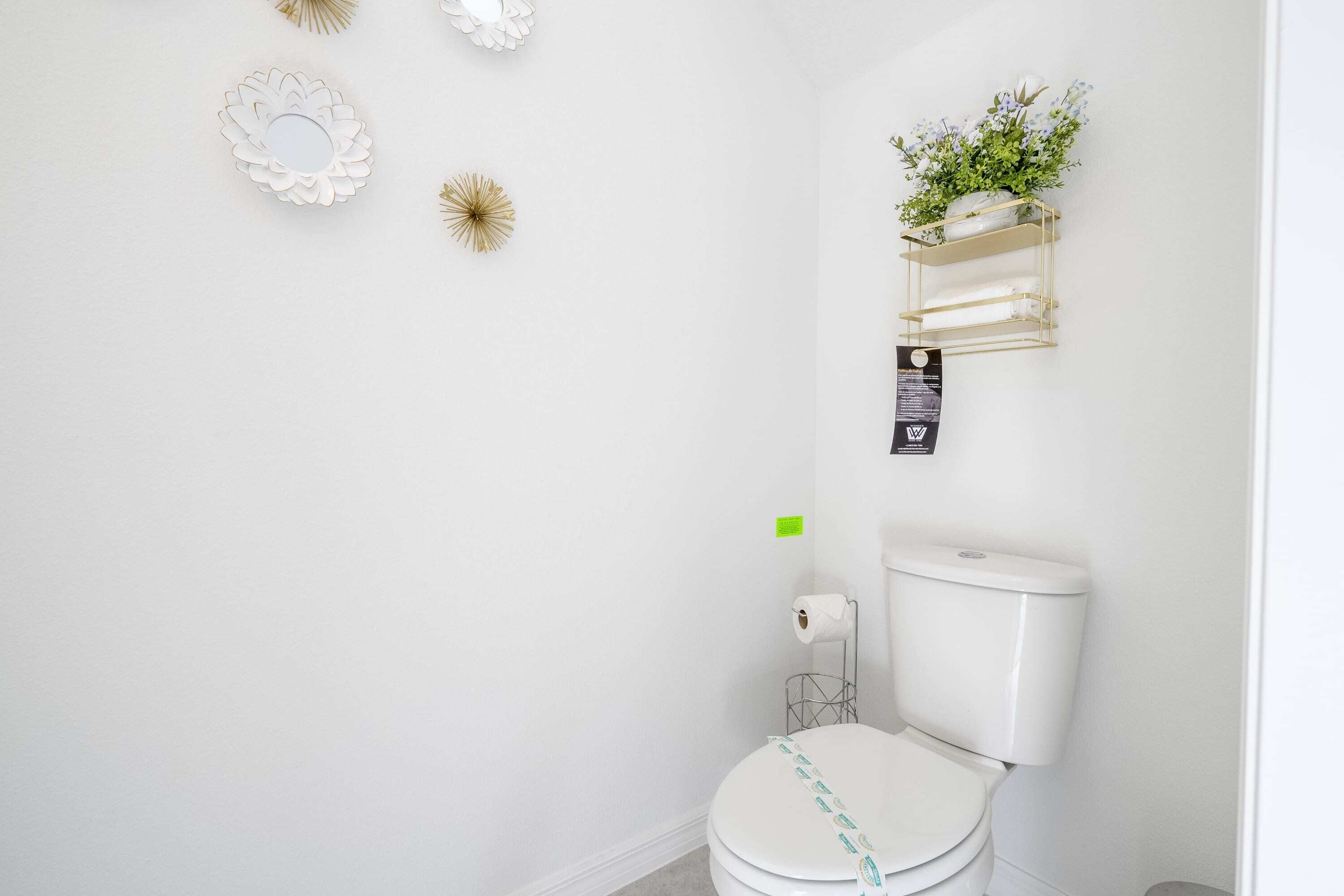 Une salle de bain avec des toilettes, une étagère fixée au mur ornée d’une plante et des éléments décoratifs sur le mur.