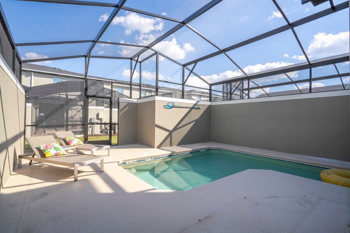 An indoor swimming pool with a glass ceiling, lounge chairs, and a view of the sky.