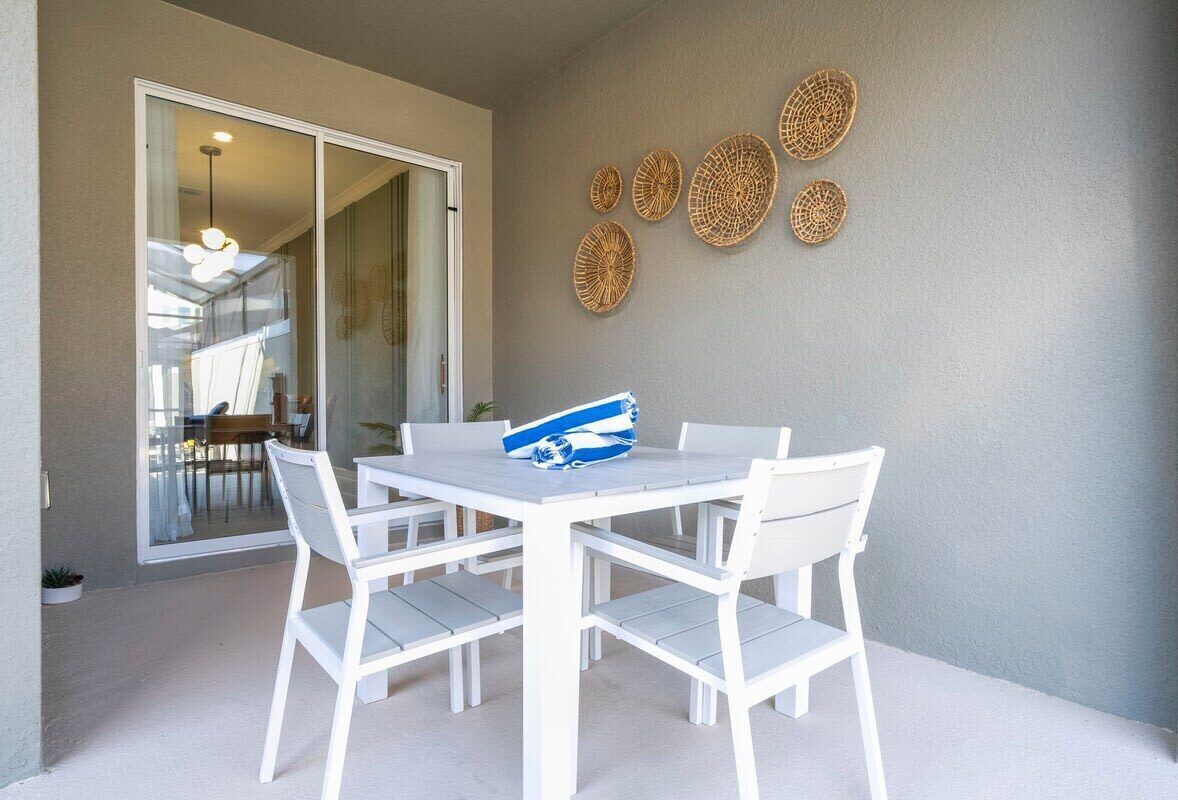 A white table and chairs set on a balcony with a sliding glass door leading to an indoor area.