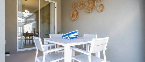 A white table and chairs set on a balcony with a sliding glass door leading to an indoor area.