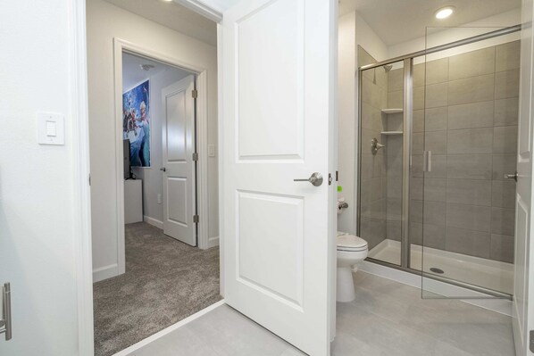 A modern bathroom with a glass shower enclosure, a toilet, and a door leading to another room. - Fantastic 4 Bd W/ Pool @ Storey Lake Resort 2709 (Kissimmee)