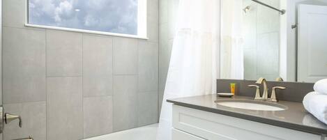 A modern bathroom with a bathtub, a window with a view of the sky, a sink with a mirror, and a shower curtain.