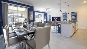 A modern kitchen with a central island, a dining area with a large table, and a view of the outdoors through a sliding door. - Fantastic 4 Bd W/ Pool @ Storey Lake Resort 2709 (Kissimmee)