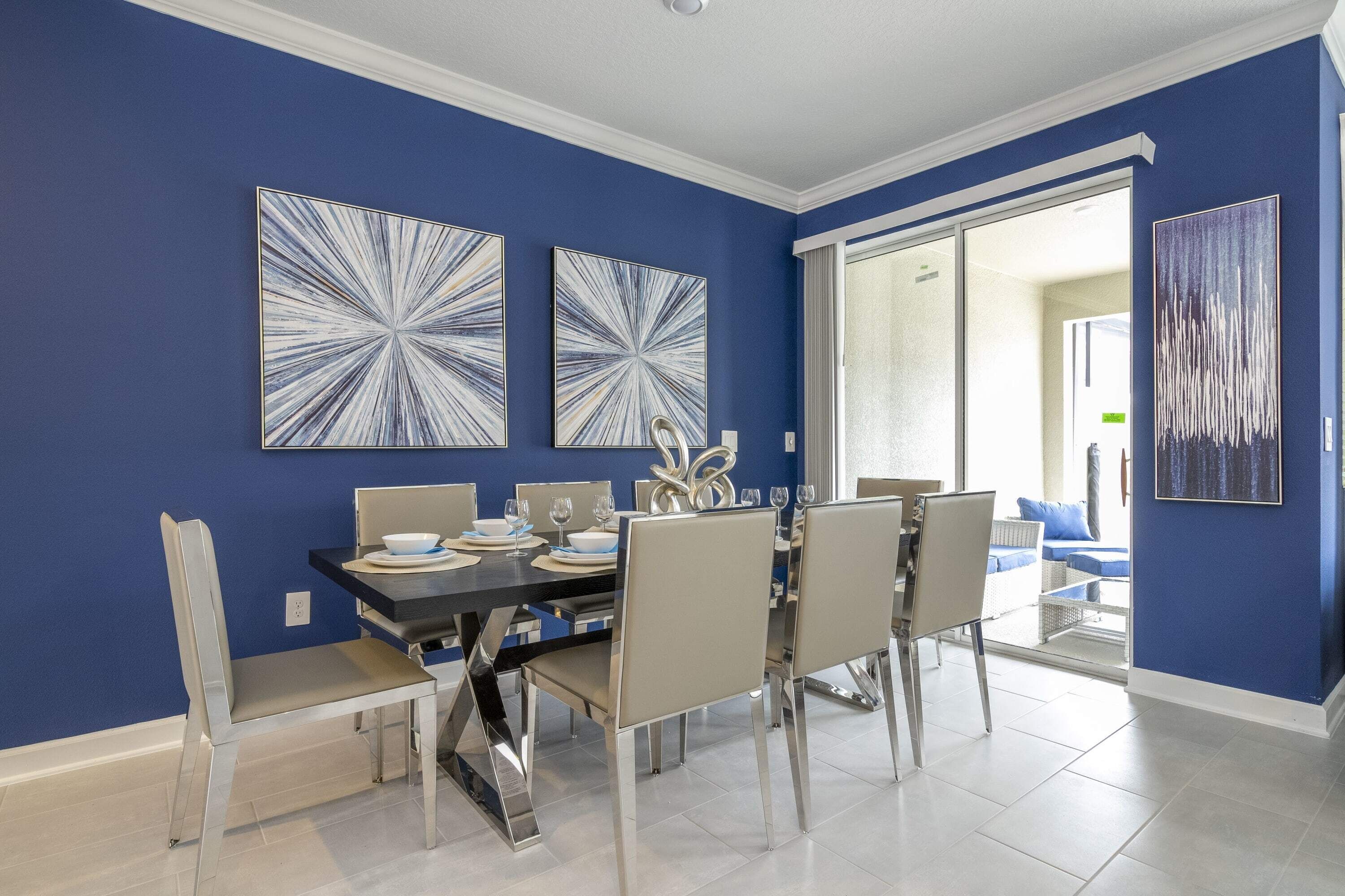 A dining area with a blue wall, modern chairs, a black table, and abstract art.