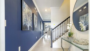 A hallway with blue walls, a glass console table, and a staircase with a black railing. - Fantastic 4 Bd W/ Pool @ Storey Lake Resort 2709 (Kissimmee)