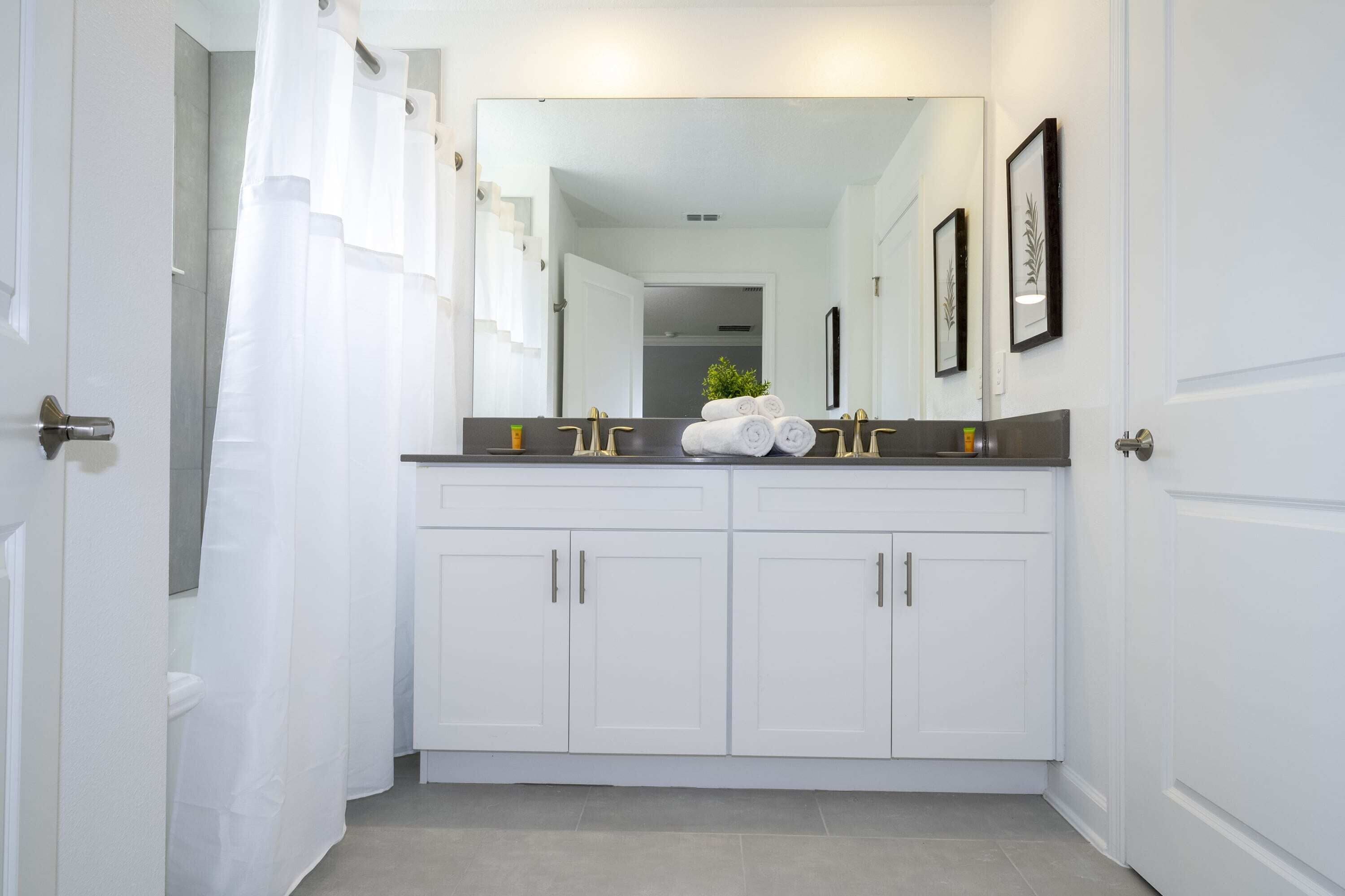 Een moderne badkamer met witte kastjes, een grote spiegel en een douchegordijn.