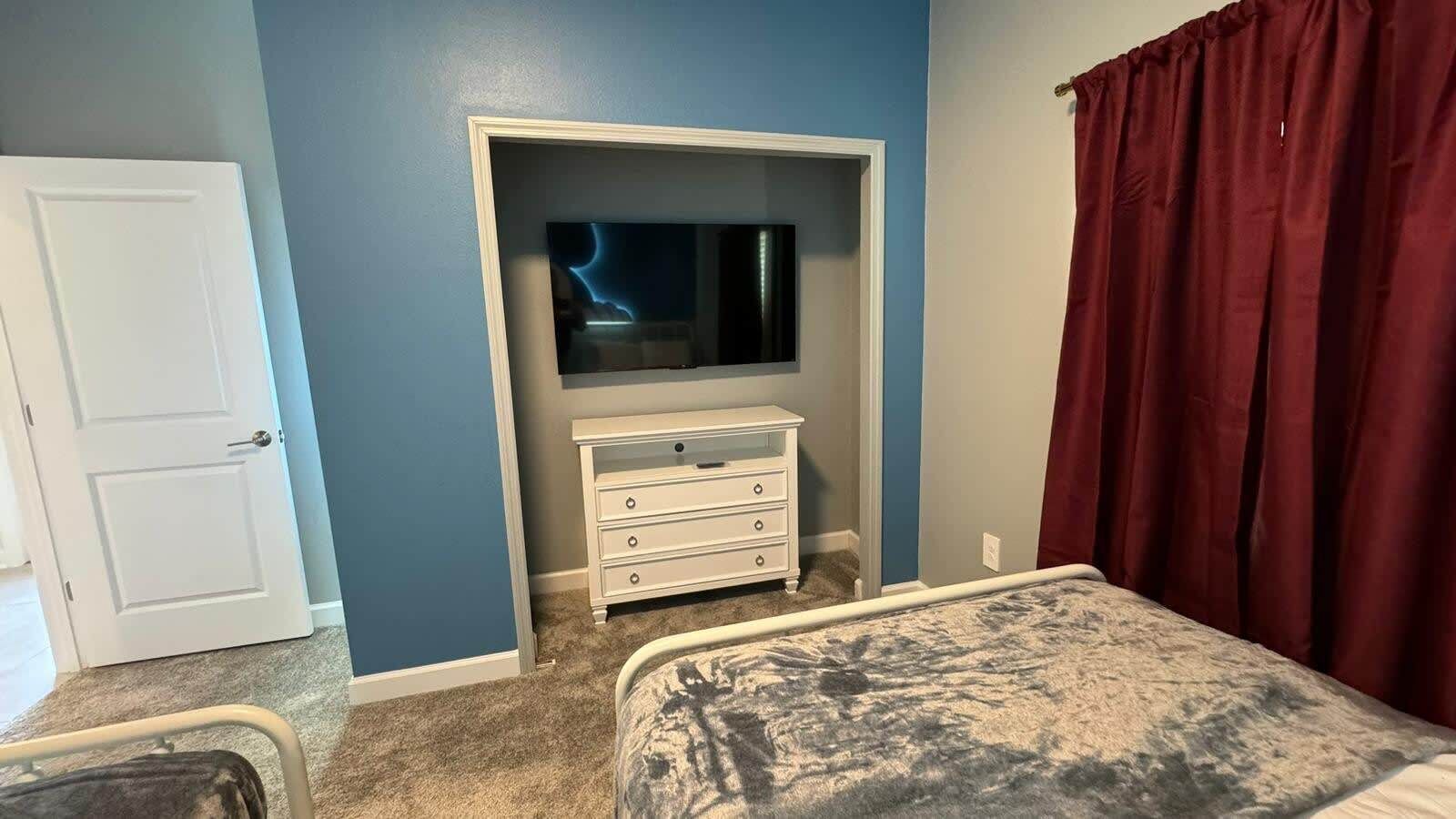 Un dormitorio con cama, cómoda, televisor y puerta.