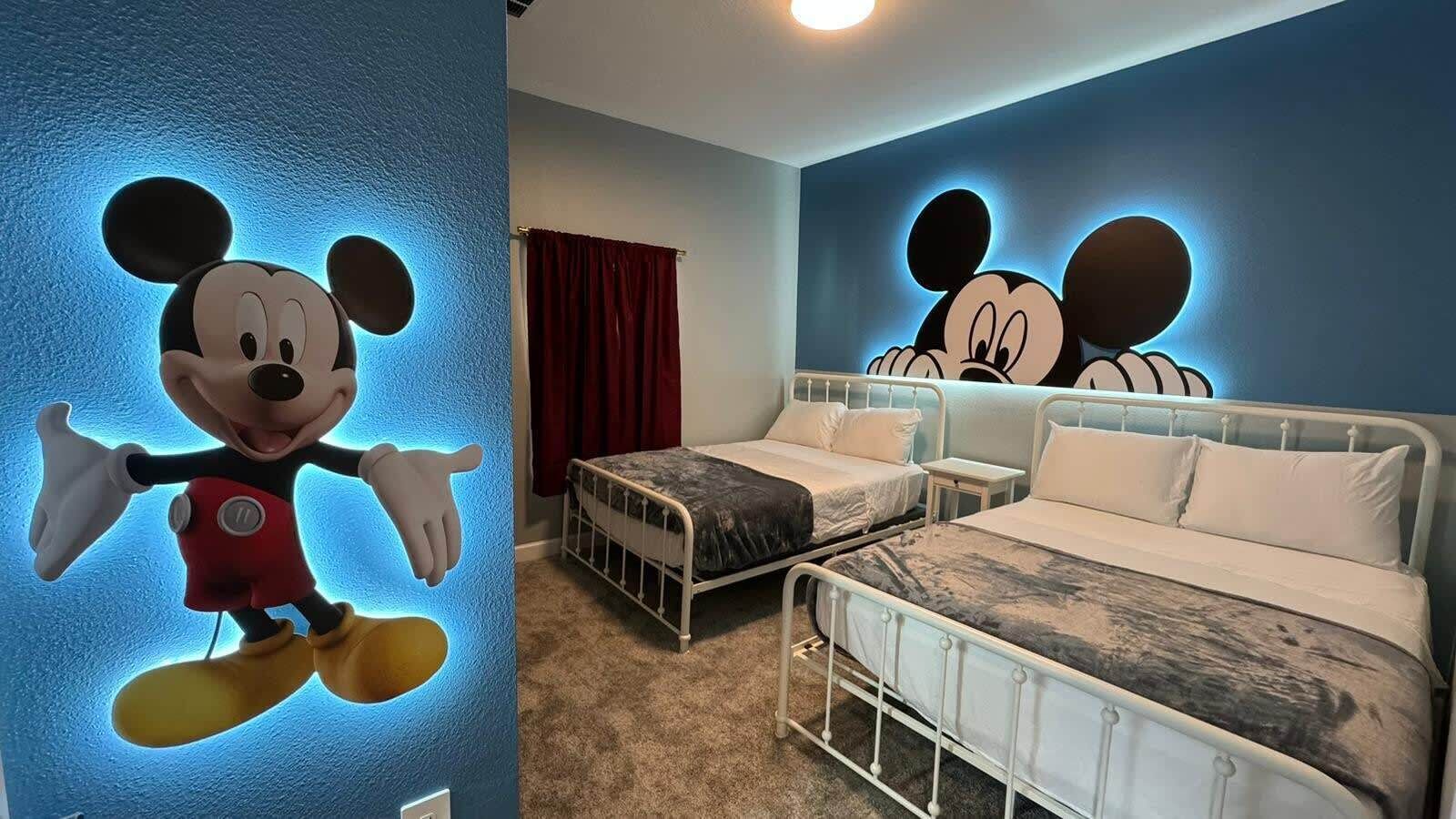 A hotel room with two beds, a Mickey Mouse mural, and a red curtain.