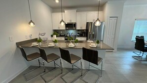 Una cocina moderna con armarios blancos, electrodomésticos de acero inoxidable y una isla central con taburetes de bar.