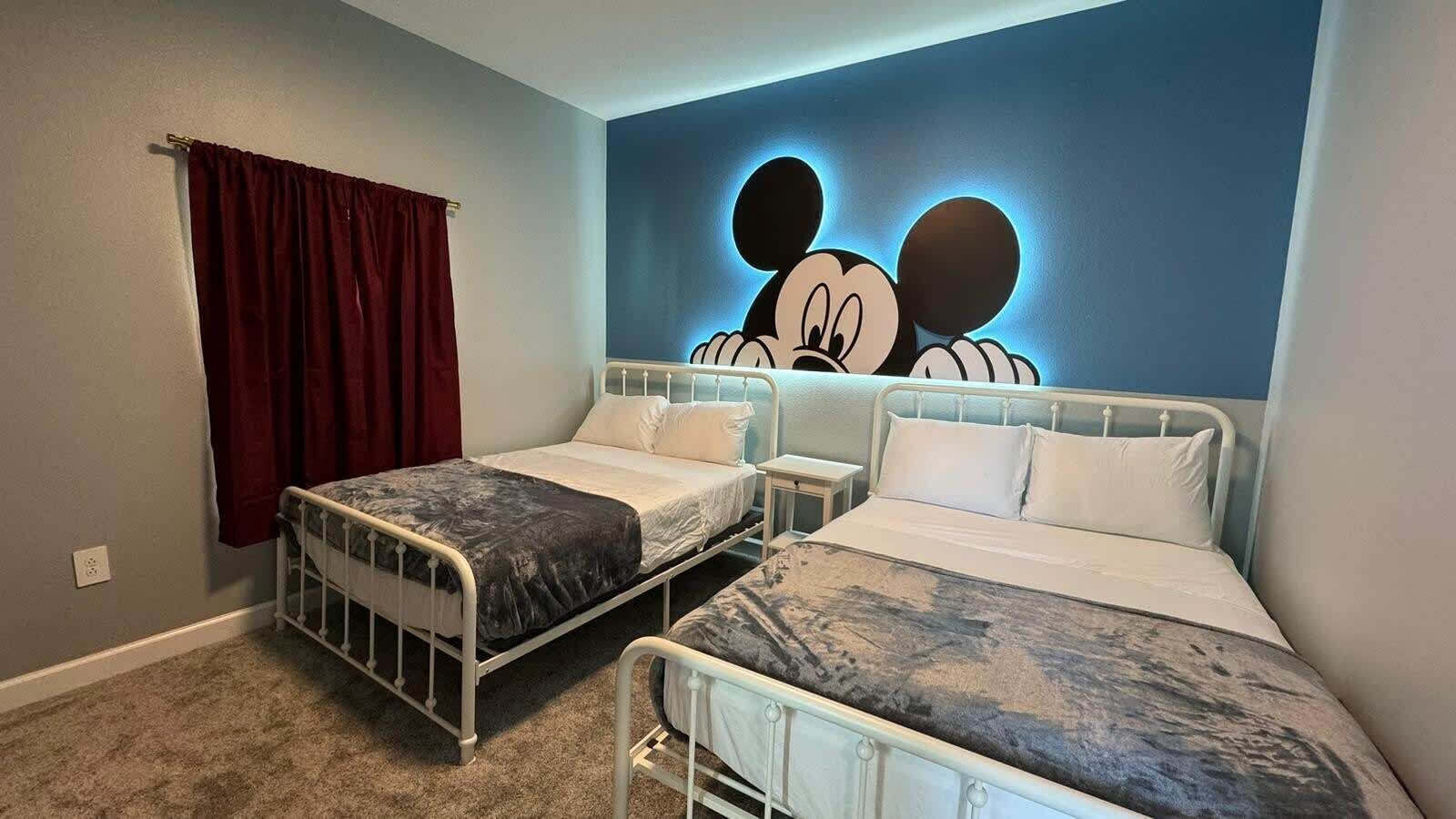 Una habitación con dos camas, una cortina roja y un mural de Mickey Mouse en la pared.
