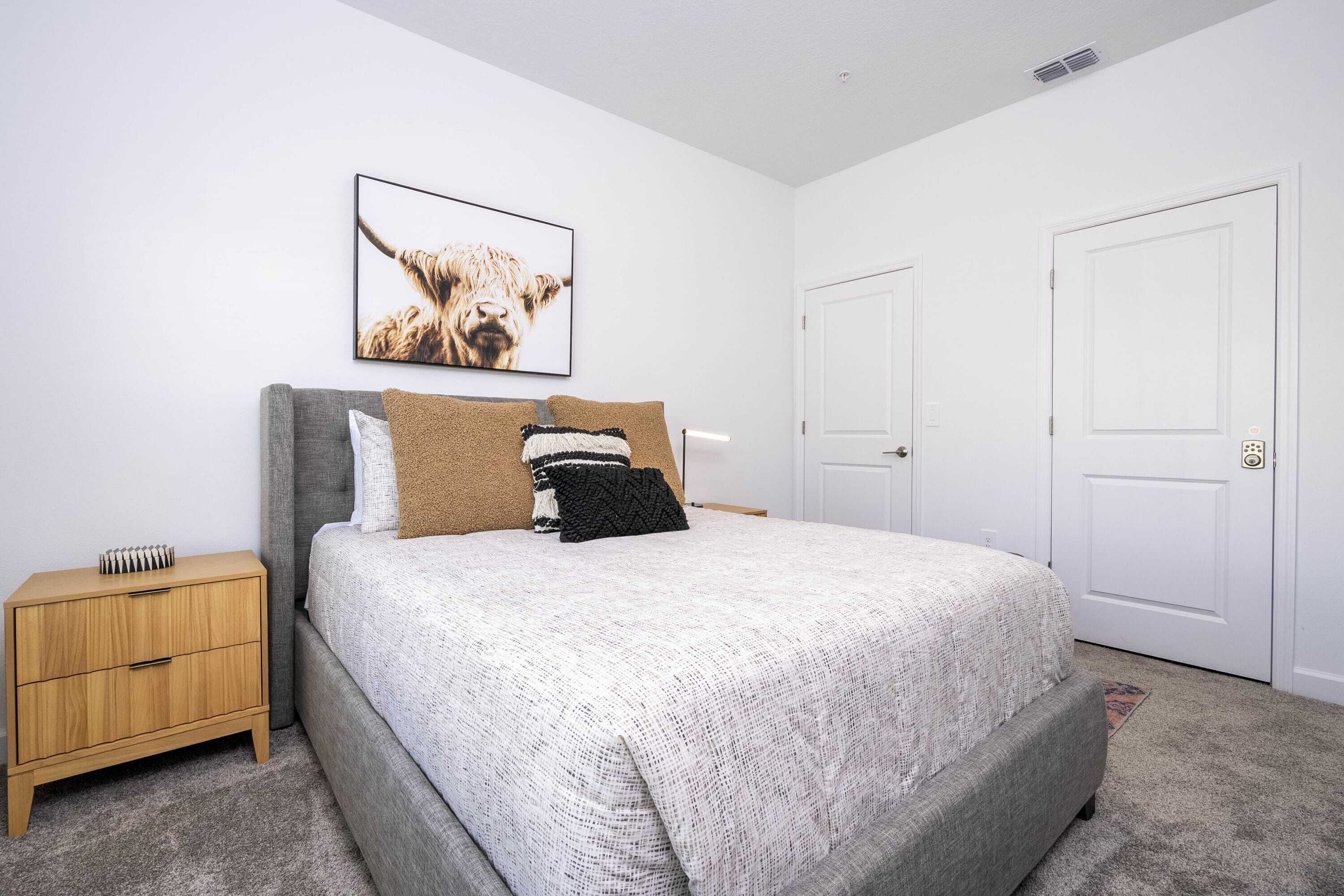 A bedroom with a bed, a nightstand, a framed picture on the wall, and two doors.
