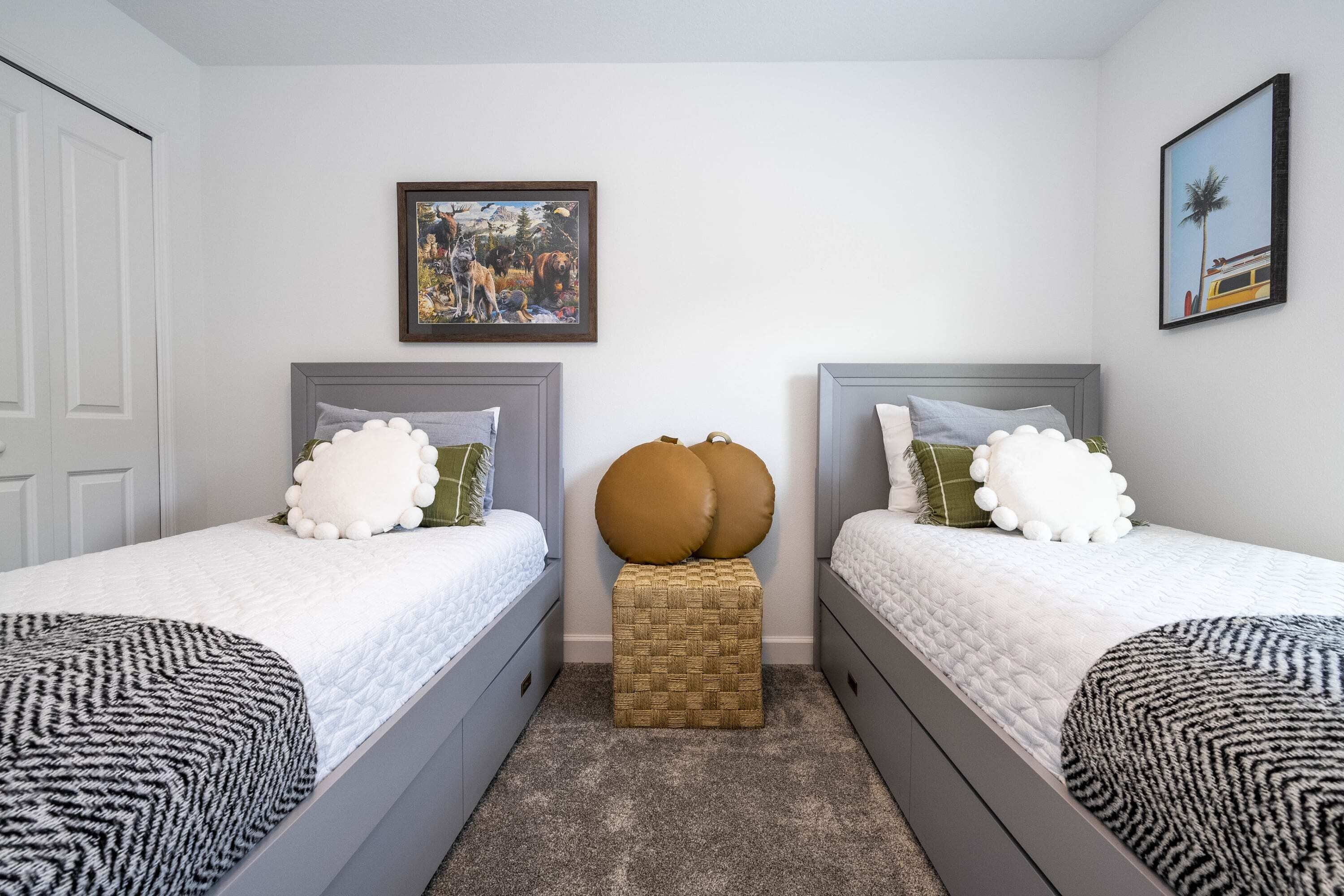 Une chambre avec deux lits, un pouf en osier et un tableau encadré au mur.