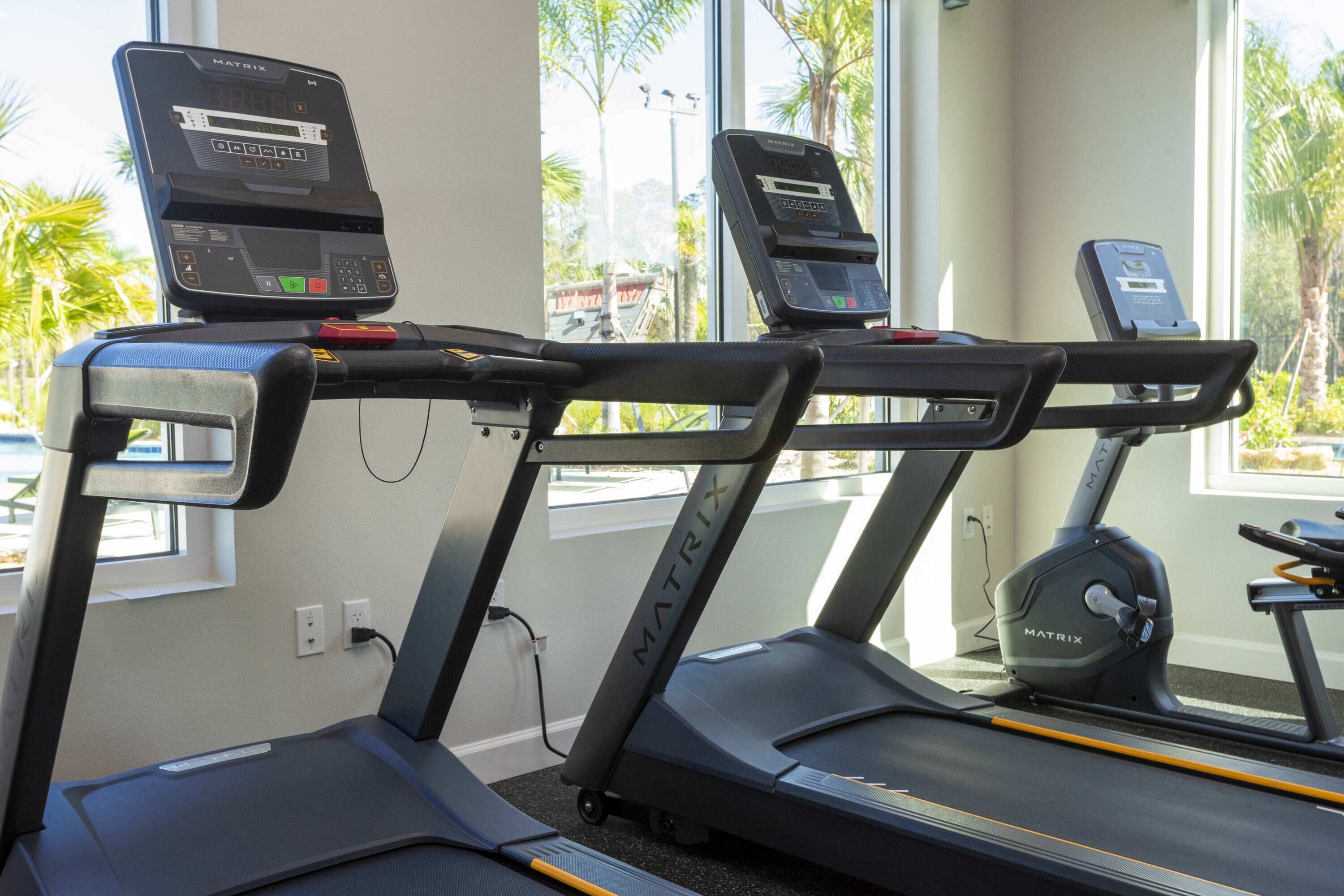 Three MATRIX treadmills in a room with large windows and a view of palm trees outside.