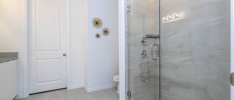 A modern bathroom with a glass-enclosed shower, a white toilet, and decorative wall art.