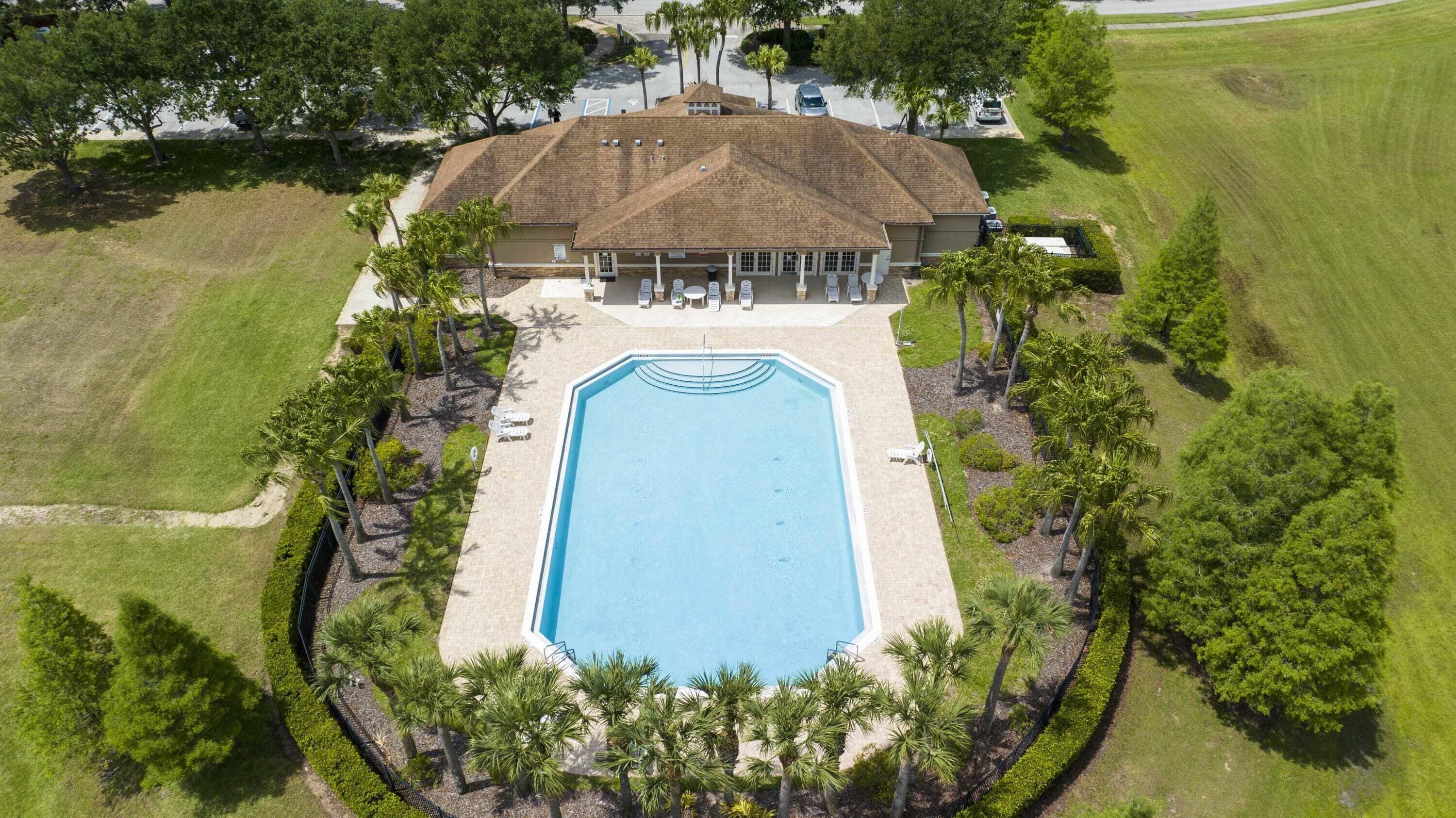 An aerial view of a house with a swimming pool, surrounded by a well-maintained lawn and palm trees.