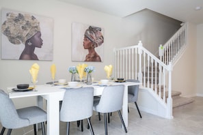 A dining area with a white table, grey chairs, and yellow napkins. There are two paintings on the wall and a staircase with white railings. - Gorgeous 5Bd W/ Pool At Windsor Island Resort 3882 (Davenport)