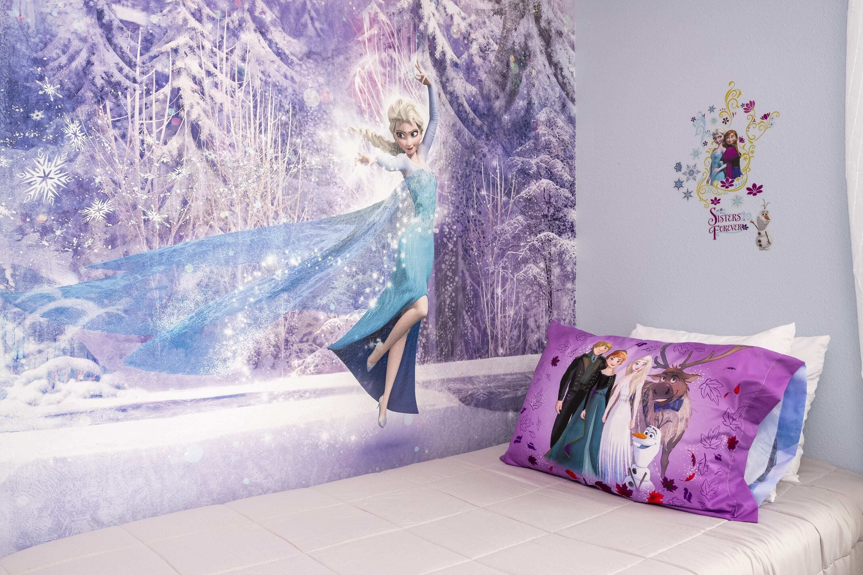 A bedroom with a bed, a wall mural, and a pillow with Frozen characters.