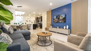 Un salon moderne avec un canapé d’angle, une table basse ronde et un coin repas à l’arrière-plan.