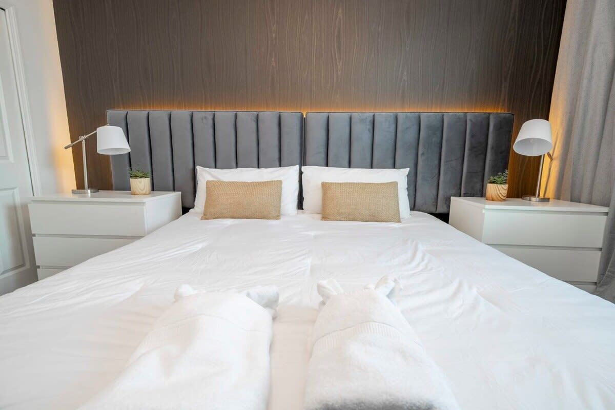 A modern hotel room with a large bed, two bedside tables, and a headboard with built-in lighting.