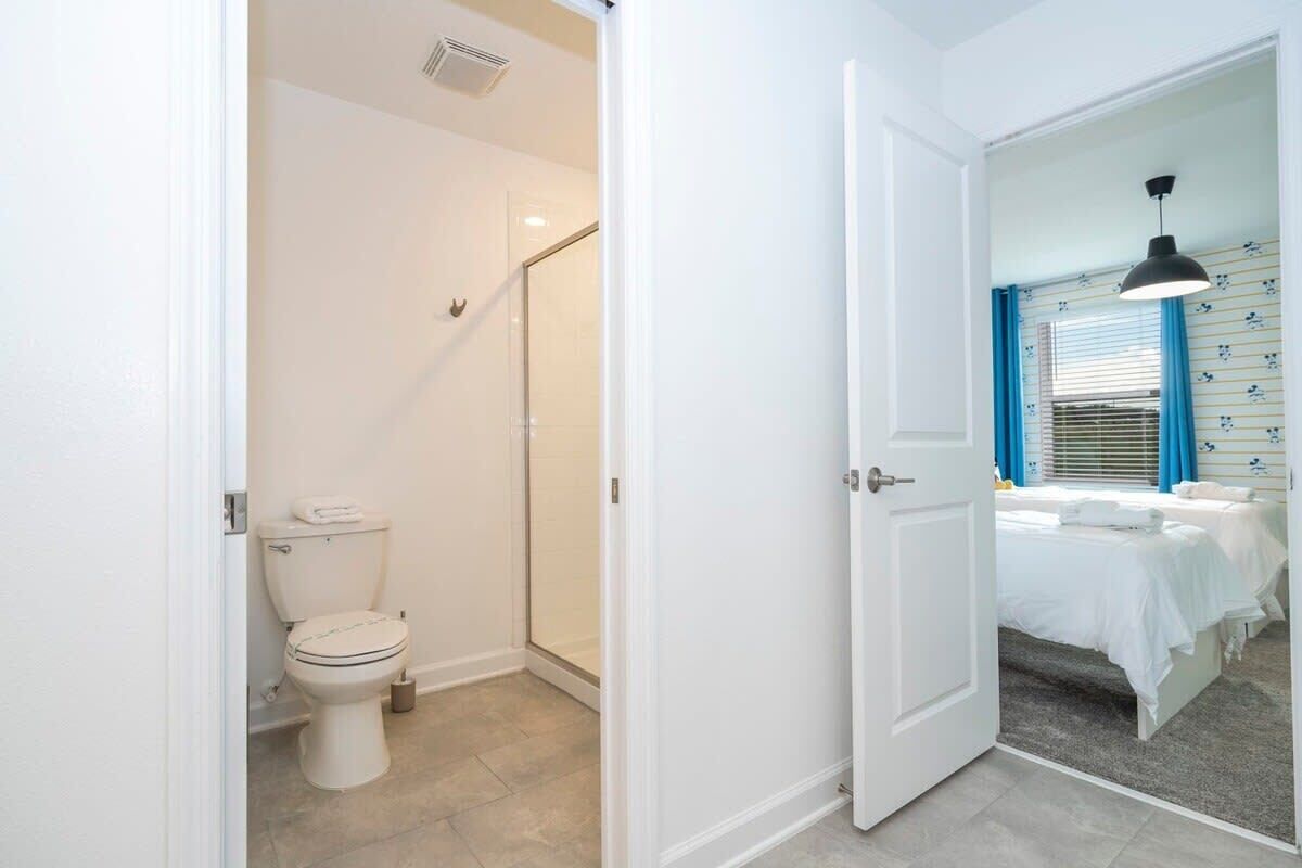 A bathroom with a toilet, shower, and a bed with a nightstand.
