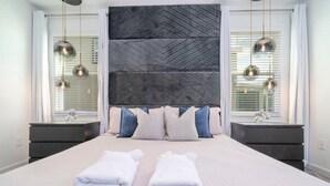 Een moderne slaapkamer met een groot bed, twee nachtkastjes en een decoratief wandpaneel.