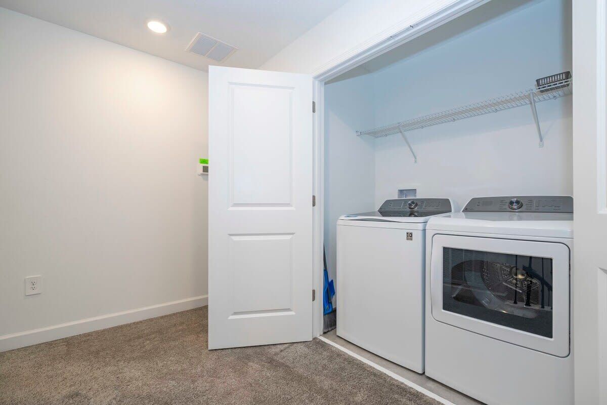 A laundry room with a white door, two stacked washers and dryers, and a metal shelf above the dryers.