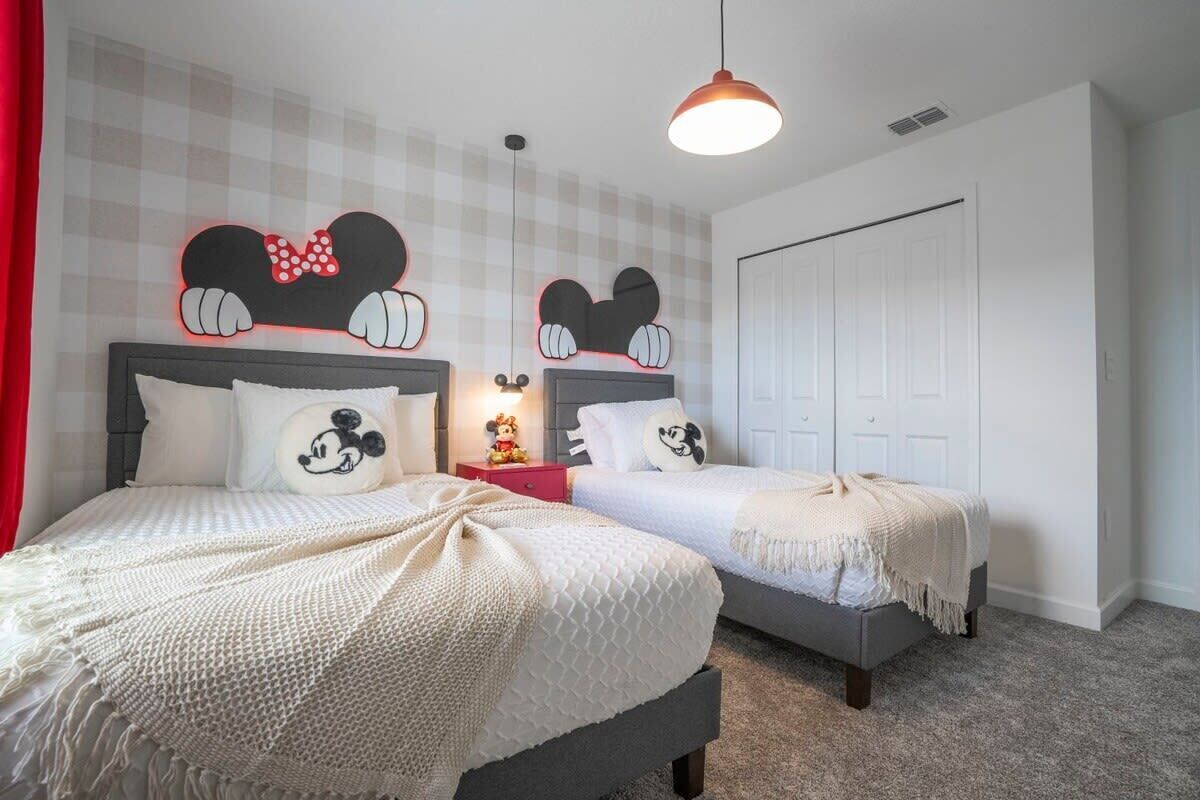 Een slaapkamer met twee bedden, een Mickey Mouse decoratie boven elk bed en een rode nachtkastje met een Mickey Mouse beeldje.