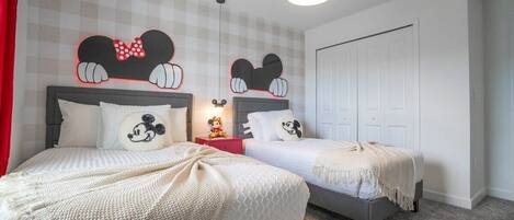 Een slaapkamer met twee bedden, een Mickey Mouse decoratie boven elk bed en een rode nachtkastje met een Mickey Mouse beeldje.