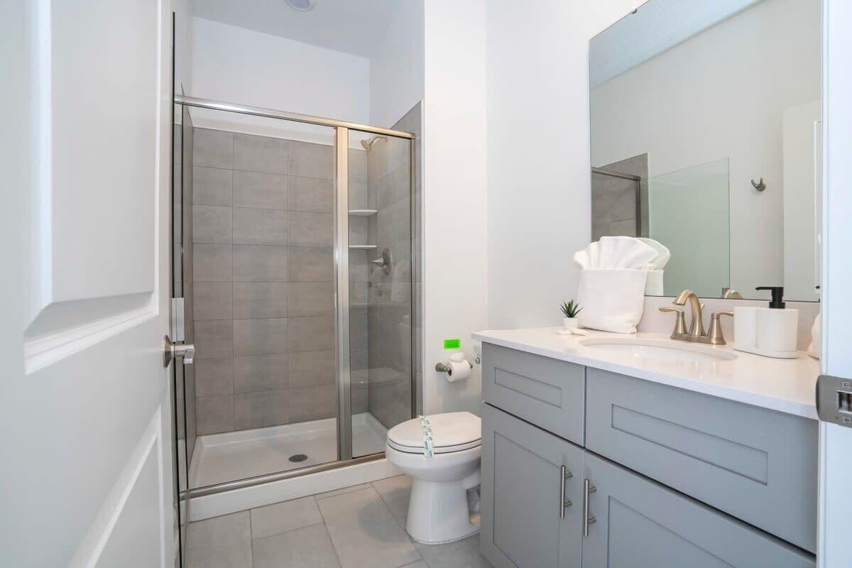 A modern bathroom with a glass-enclosed shower, a toilet, and a vanity with a mirror and sink.