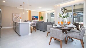 A modern kitchen with a central island, grey sofas, and a dining area with a round table and chairs.