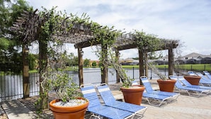 Ett utomhusområde med sittplatser, solstolar och krukväxter under en pergola.
