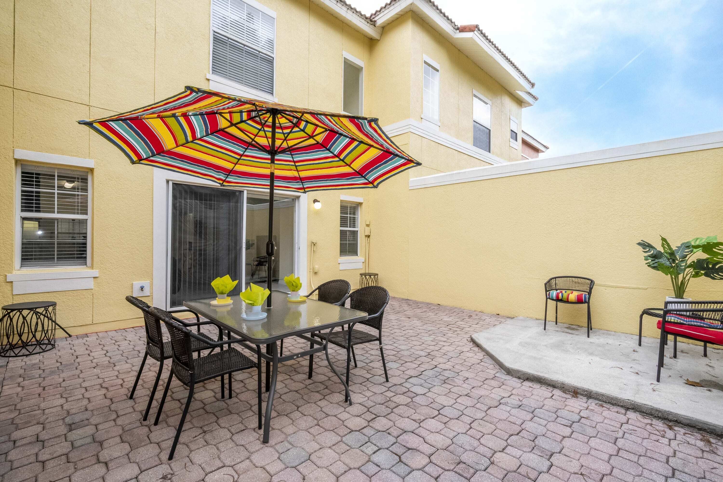 Een terras met een tafel, stoelen, een gestreept parasol en een bloempot.