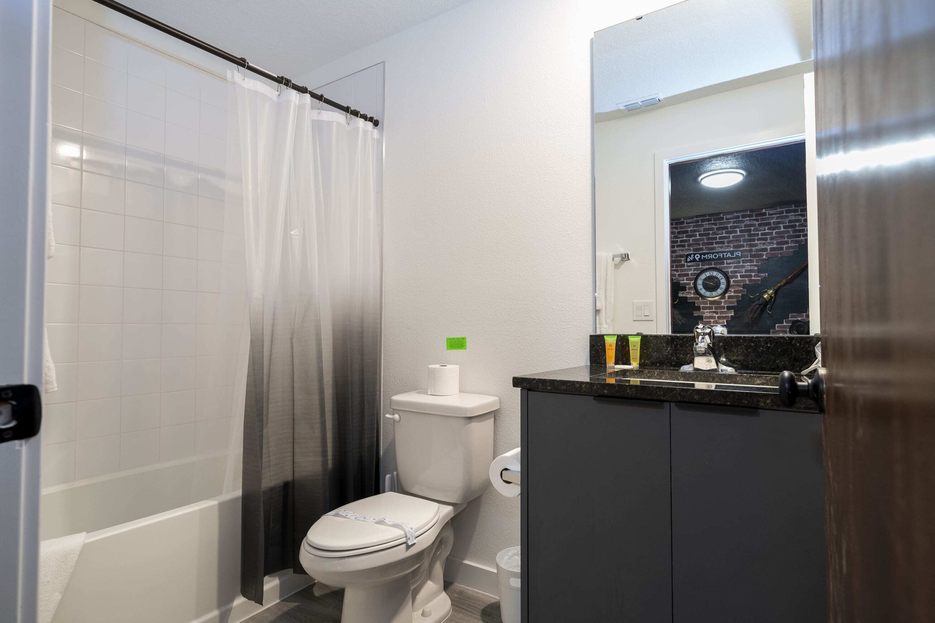 A bathroom with a toilet, a shower curtain, a bathtub, a sink, and a mirror.