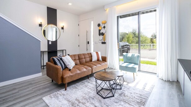 A modern living room with a leather sofa, a round coffee table, and a large sliding glass door leading to a balcony.