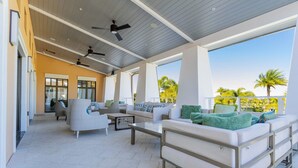 A covered outdoor lounge area with seating, ceiling fans, and large windows offering views of palm trees. - Splendid 6Bd W/ Pool At Solara Resort 2154 (Kissimmee)