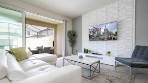 A modern living room with a white sofa, a gray armchair, a white coffee table, and a flat-screen TV mounted on a textured wall. - Splendid 6Bd W/ Pool At Solara Resort 2154 (Kissimmee)
