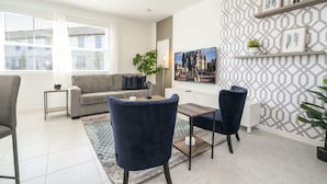 A modern living room with a grey sofa, blue chairs, a coffee table, and a TV on the wall. - Stunning 3Bd With Game Room @ Enclaves Resort 1021 (Davenport)