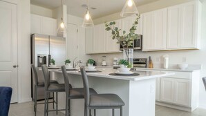 A modern kitchen with white cabinets, a central island with bar stools, and pendant lighting. - Stunning 3Bd With Game Room @ Enclaves Resort 1021 (Davenport)