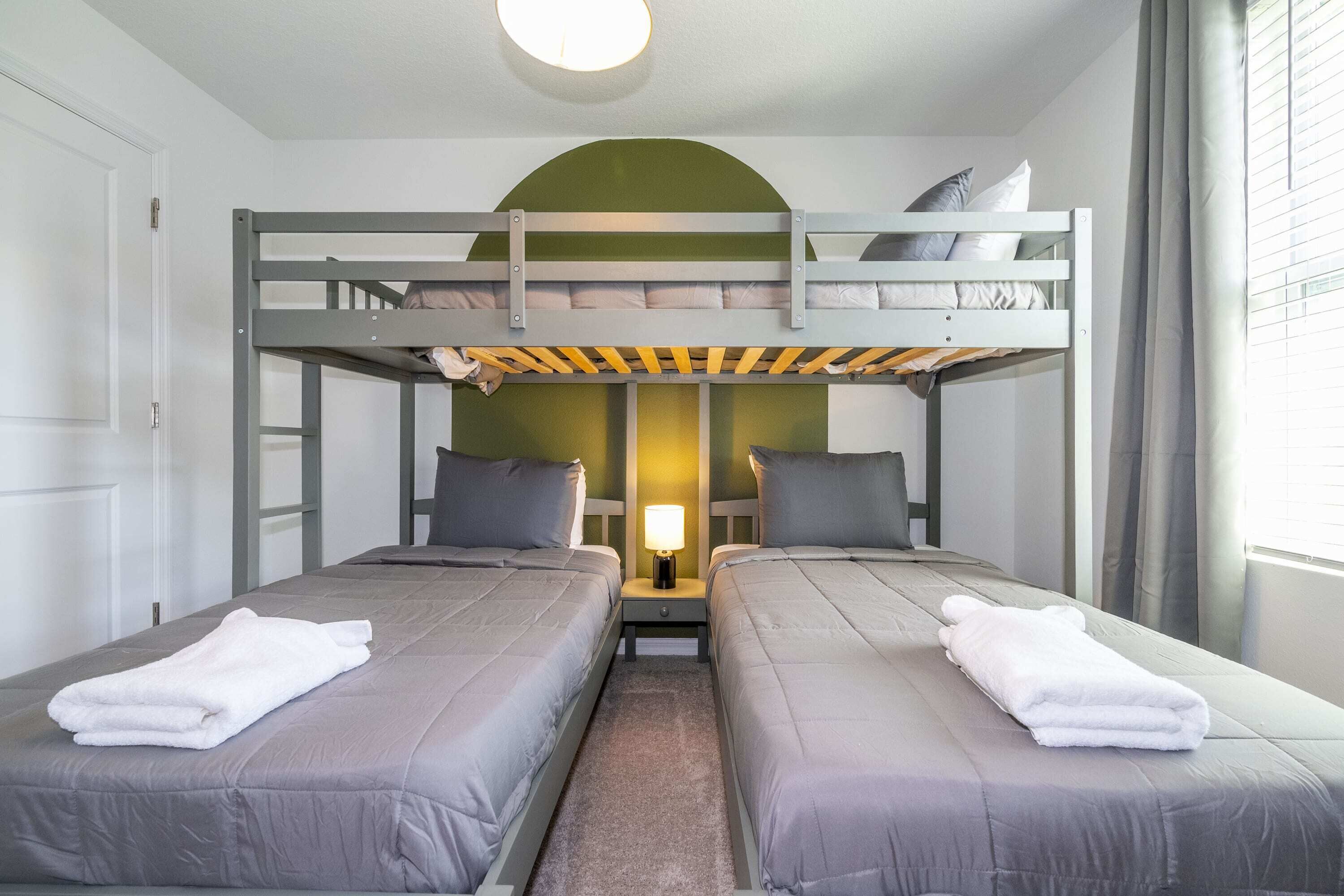 Une chambre avec un lit superposé, deux lits, une table de chevet et une lampe.