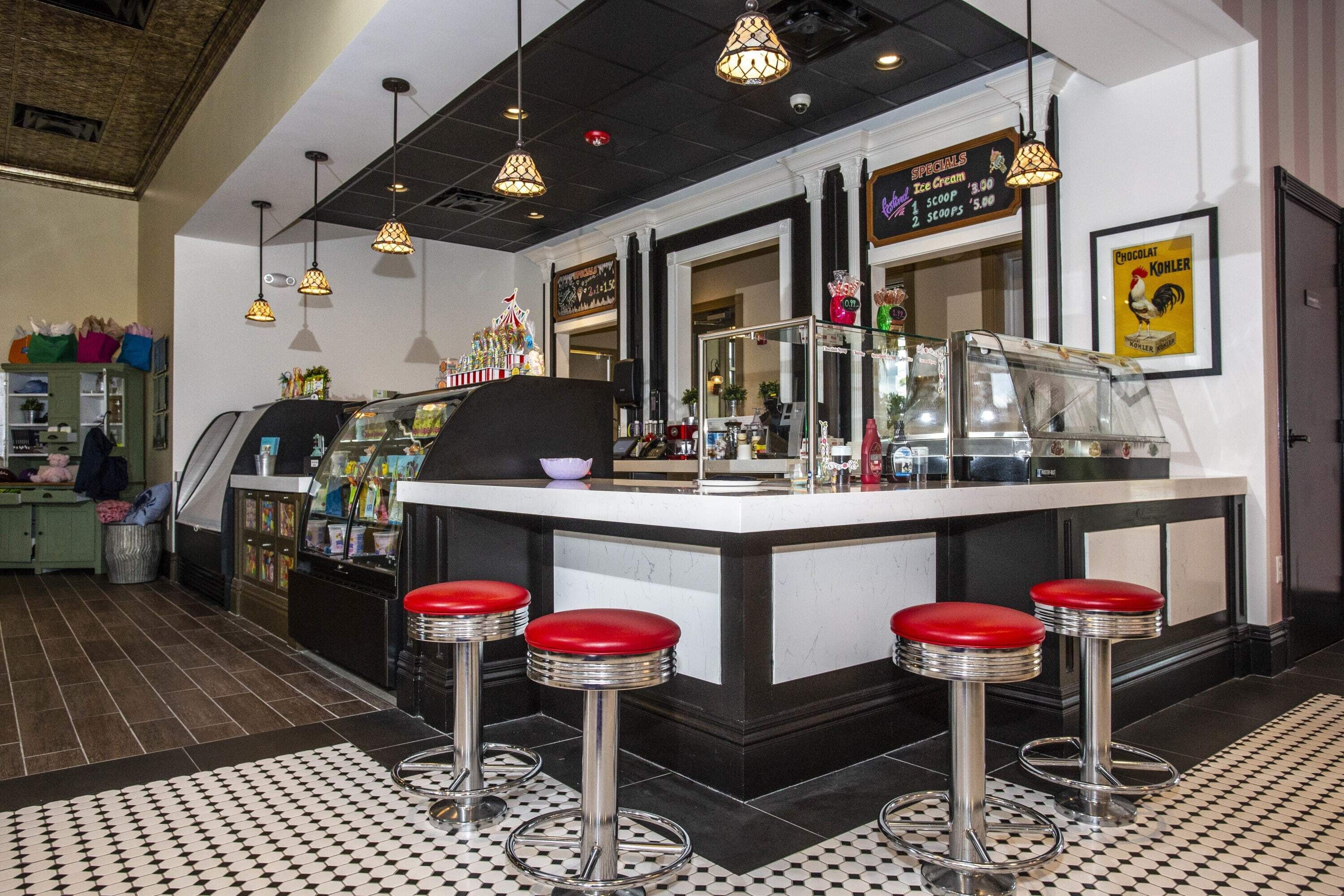 A retro-themed bar area with a central counter, red stools, and hanging pendant lights.