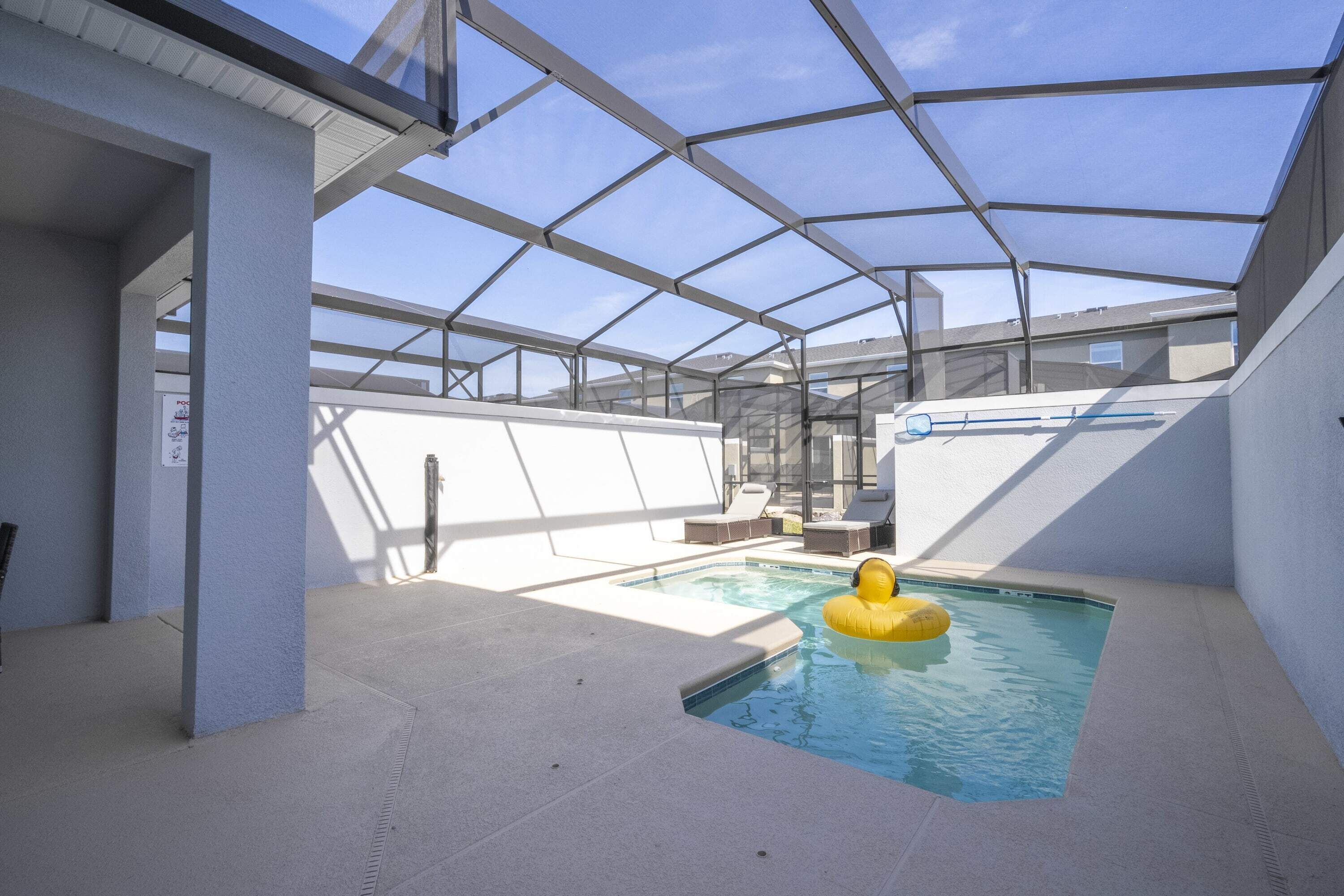 Une piscine couverte avec un flotteur jaune gonflable, un plafond en verre transparent et une vue sur les bâtiments en arrière-plan.
