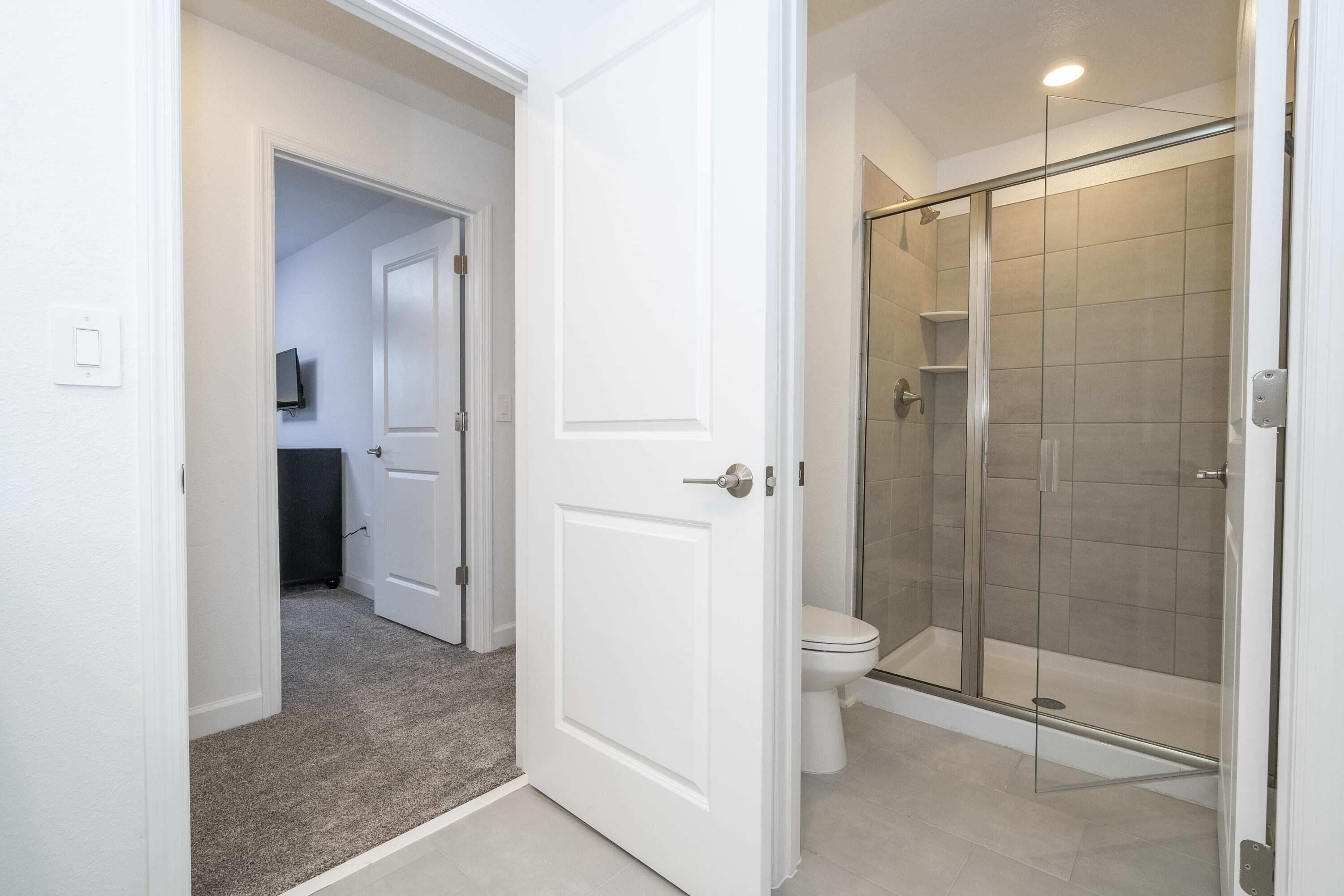 Une salle de bain avec une douche à parois de verre, des toilettes et une porte donnant sur une autre pièce.