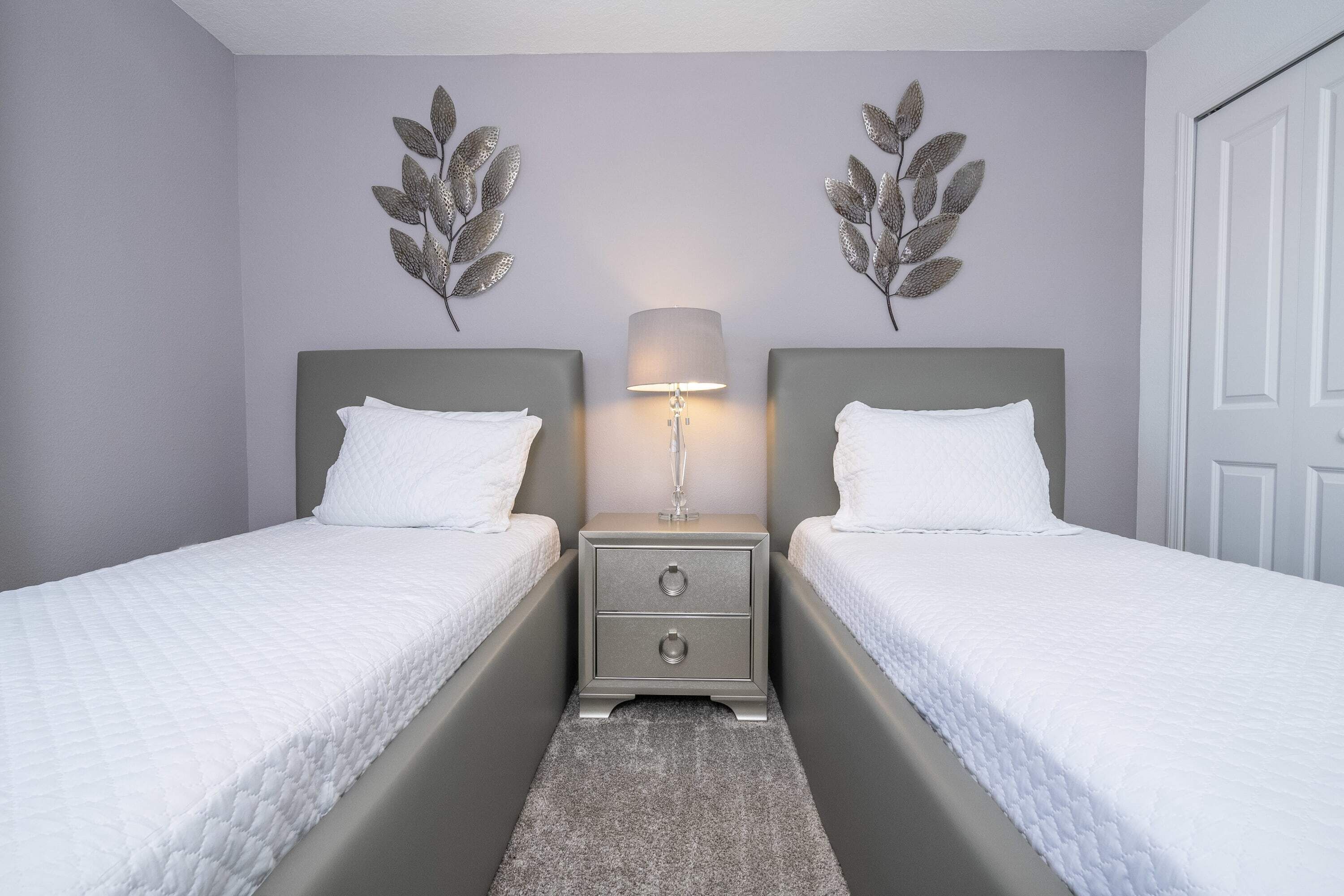 Camera matrimoniale con due letti, un comodino con lampada e decorazioni a tema foglie alle pareti.